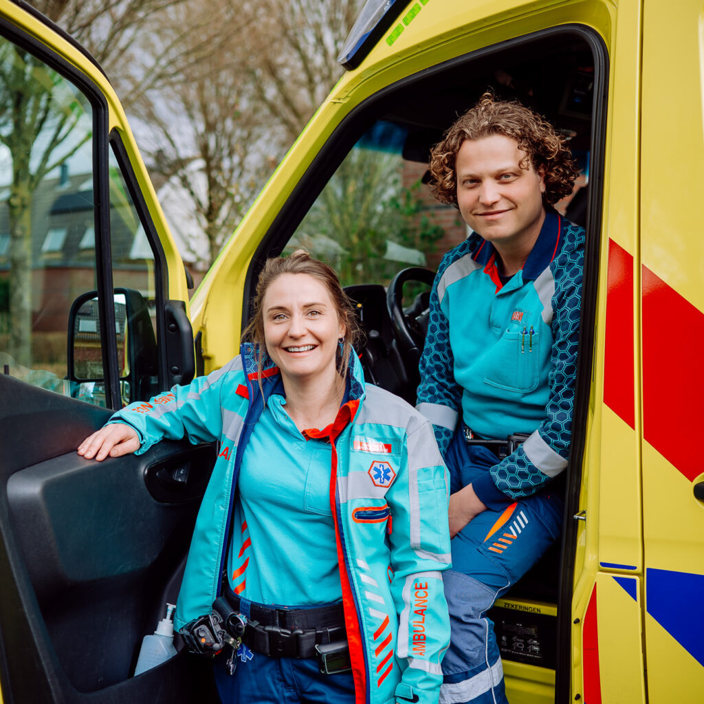 Een ambulanceteam staat in de ambulance en lacht vrolijk.