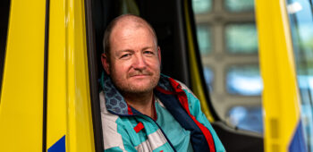 Ambulanceverpleegkundige Jorre lacht in de deuropening van de ambulance