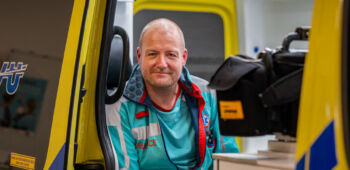 Ambulancechauffeur Jorre zit in de ambulance en lacht in de camera.
