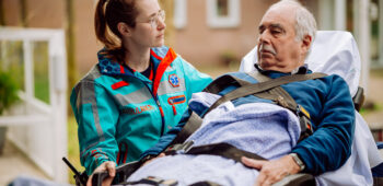 Een ambulanceverpleegkundige begeleidt een patiënt op een brancard. Lees hier hoe we op de website van de RAVU zorgen voor digitale toegankelijkheid.