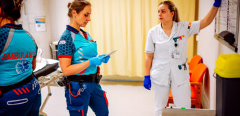 Een ambulanceverpleegkundige is bezig met de overdracht op een SEH. De SEH-verpleegkundige maakt aantekeningen op het whiteboard.