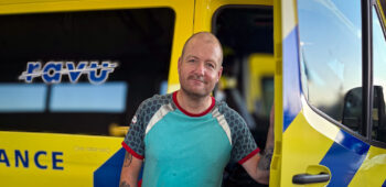 Ambulanceverpleegkundige Jorre staat voor de ambulance en lacht