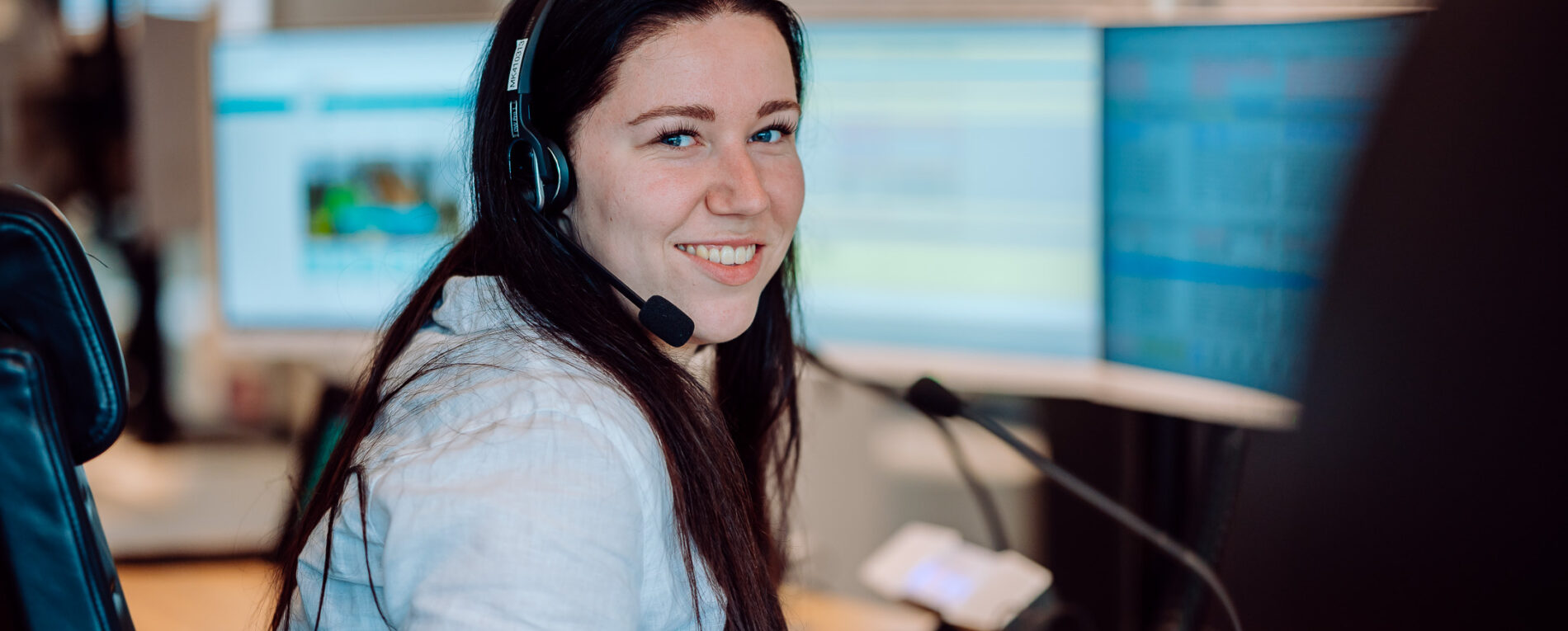 Een verpleegkundig meldkamercentralist is te zien met een headset op en een aantal schermen voor haar.