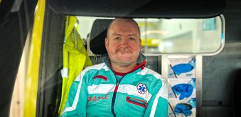 Ambulanceverpleegkundige zit in de ambulance en kijkt door de ruit naar voren.