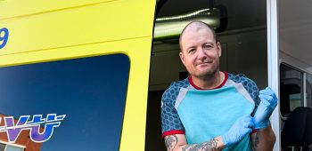 Ambulanceverpleegkundige Jorre staat in de deur van de ambulance en trekt een handschoen aan.