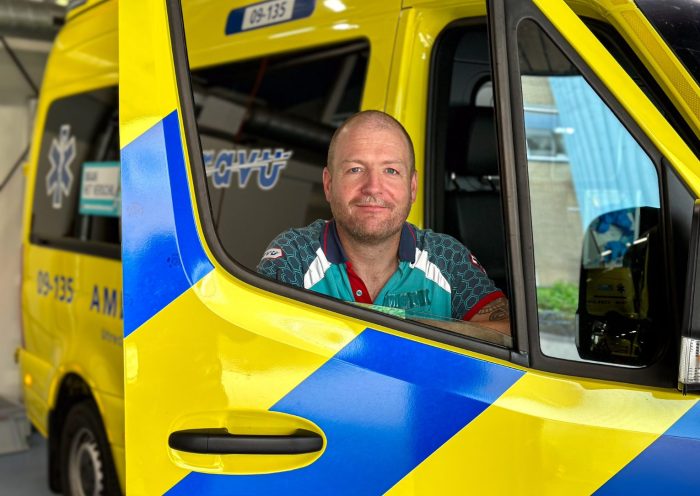 Ambulanceverpleegkundige Jorre staat in de deur en kijkt recht vooruit door het raam heen.