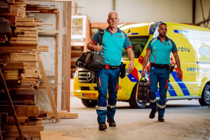 Een ambulanceteam loopt met tassen richting een hulpverlening. Op de achtergrond staat een ambulance. Lees er meer over in het jaaroverzicht van de RAVU.